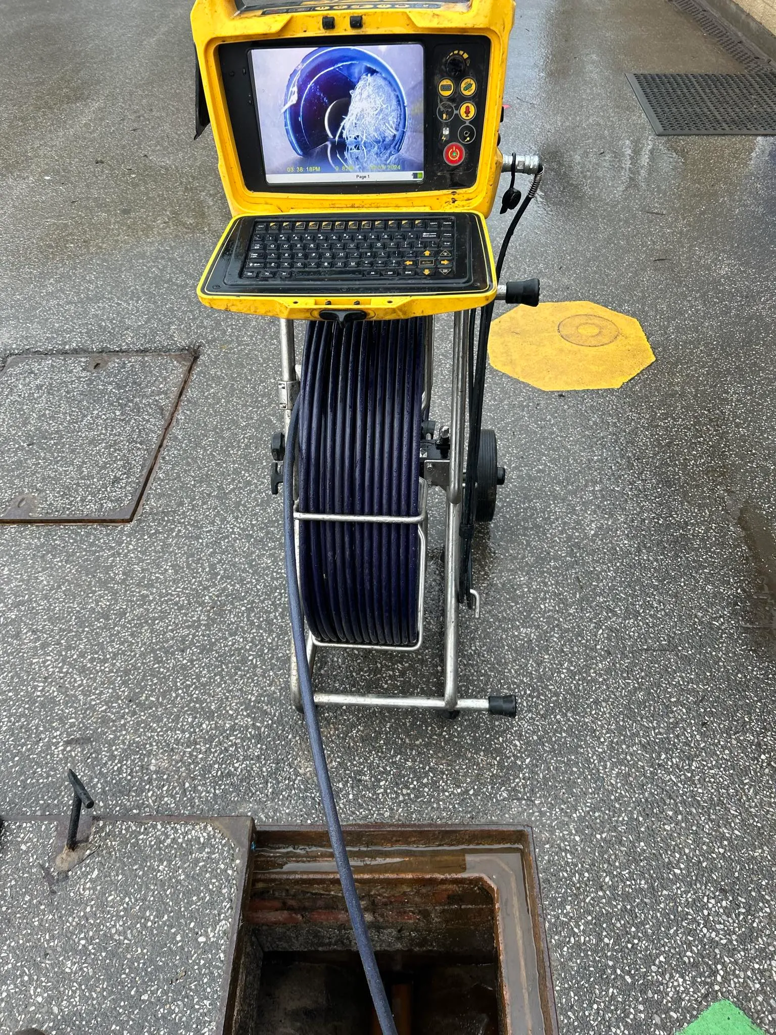 CCTV drain camera and monitor at a manhole cover, showing a blocked pipe on the screen.